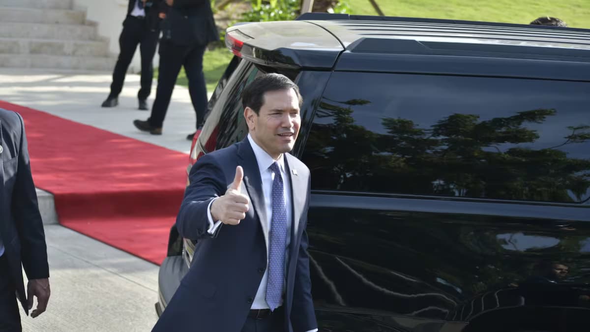 Un hombre de traje saluda con el pulgar en alto junto a una camioneta oficial sobre una alfombra roja