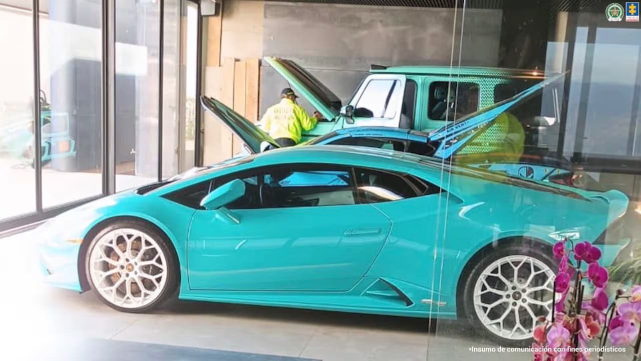 Un deportivo de color turquesa y una camioneta del mismo color dentro del garaje acristalado de una vivienda, con un uniformado de policía al fondo