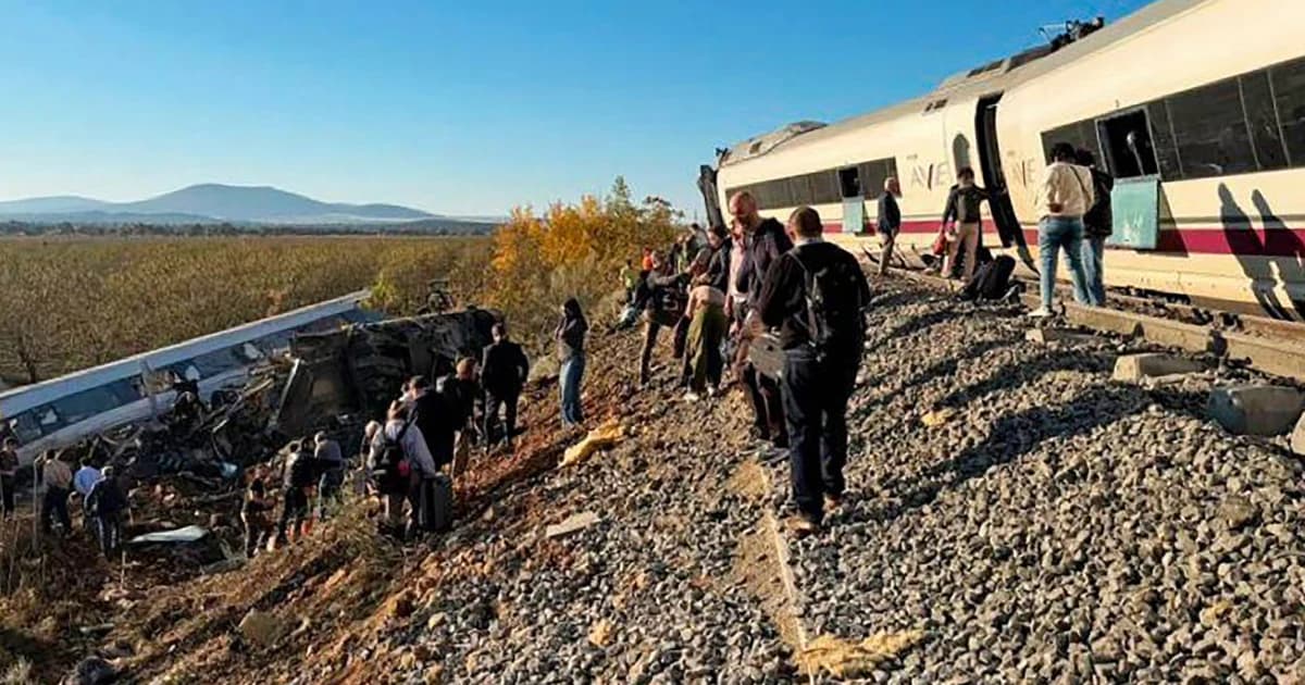 Pasajeros caminan junto a las vías al lado de un AVE detenido y de los vagones descarrilados tras el choque cerca de Urda, Toledo