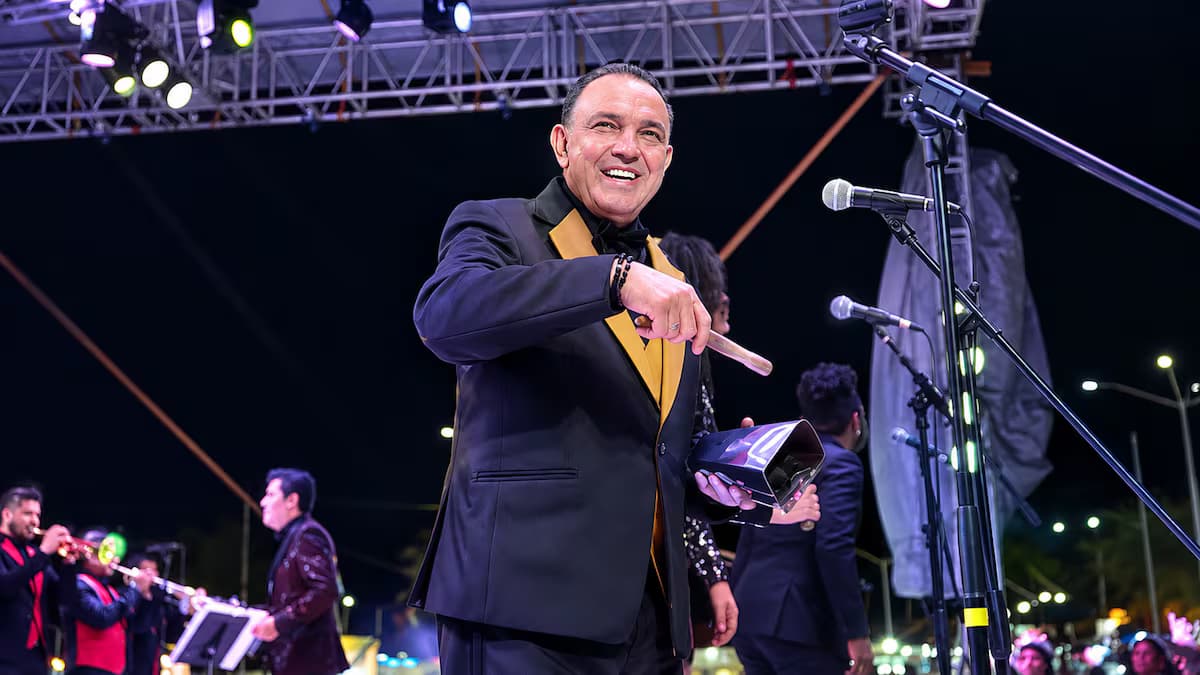 Álvaro Pava sonríe en una tarima con un cencerro en la mano, con la orquesta detrás