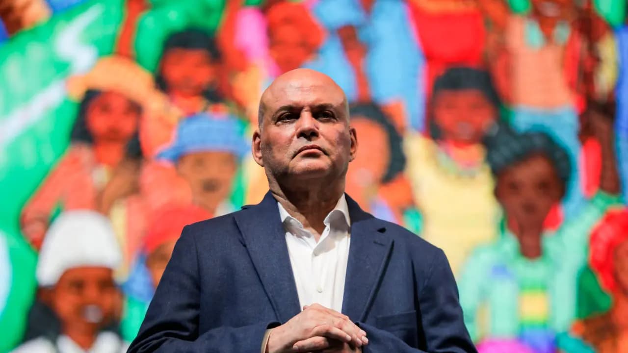 Salvatore Mancuso, de saco azul y camisa blanca, con las manos entrelazadas frente a un mural de colores
