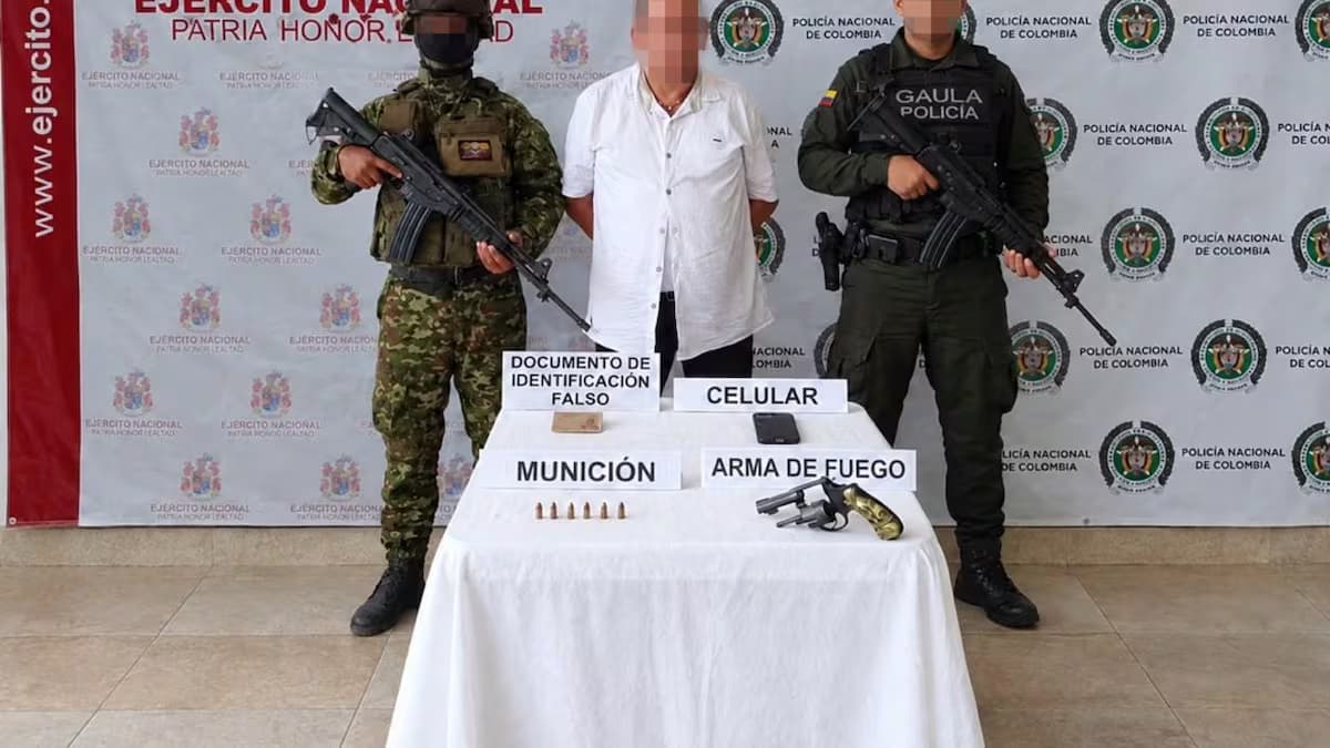 Alias Mongolo, con el rostro pixelado, custodiado por un soldado y un policía del Gaula junto al revólver, el celular y el documento falso incautados