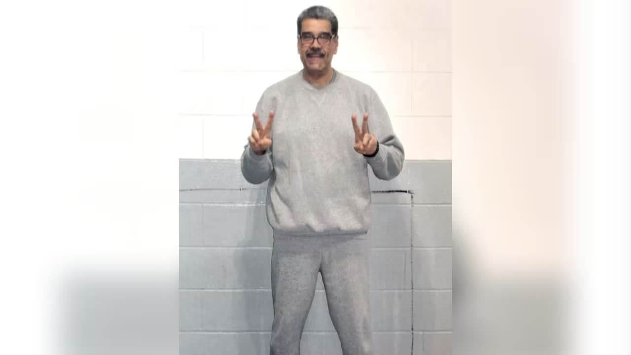 Nicolás Maduro, de pie con sudadera gris y gafas, hace la señal de victoria con las dos manos frente a un muro de bloques