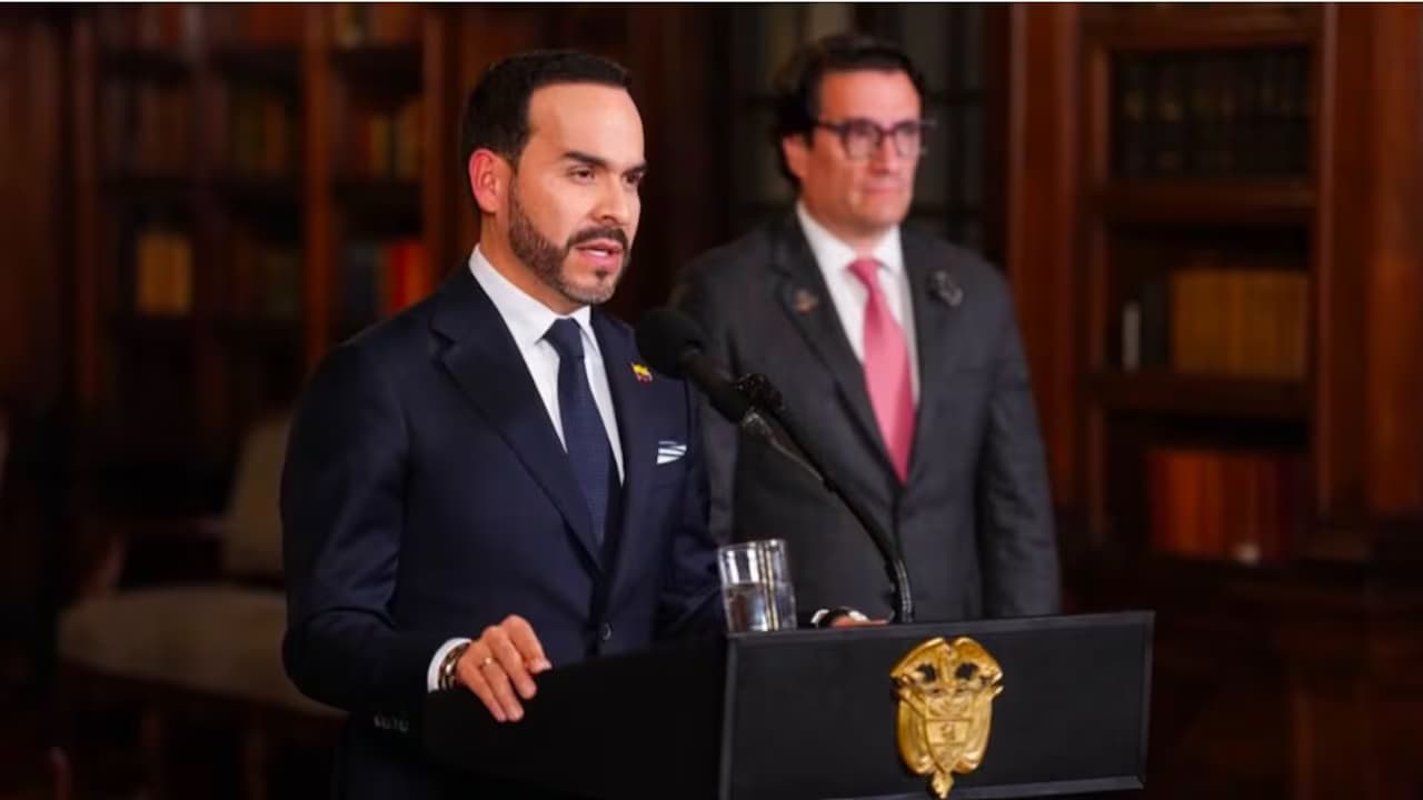 El presidente Abelardo de la Espriella habla ante un micrófono en un atril con el escudo de Colombia, acompañado por un funcionario en una sala con bibliotecas de madera