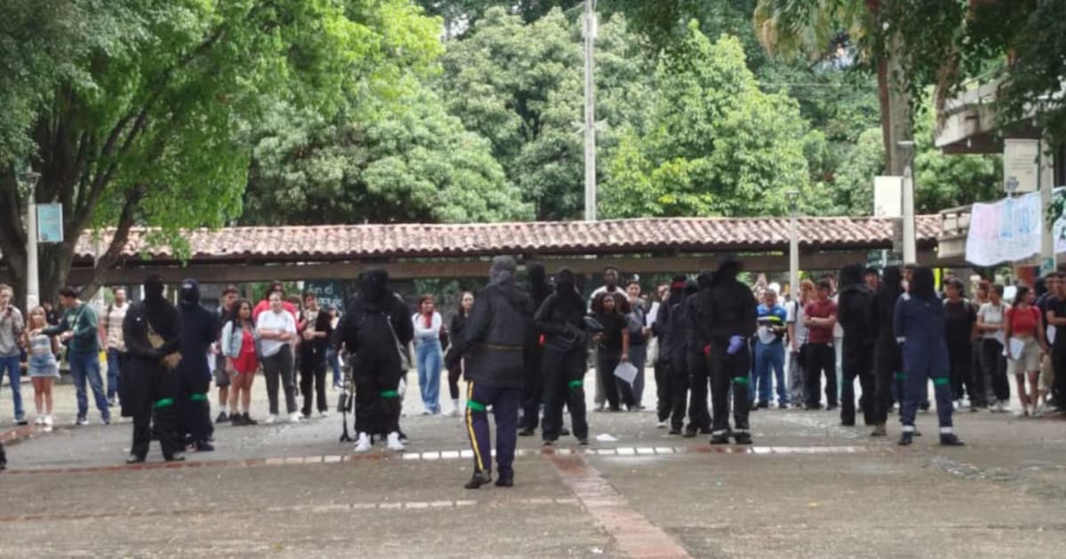 Un grupo de encapuchados camina por una plazoleta de un campus universitario ante la mirada de estudiantes