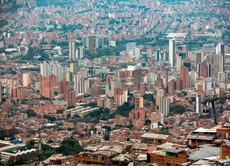 Panorámica de edificios y barrios de Medellín vista desde una ladera, con una línea de Metrocable a la derecha
