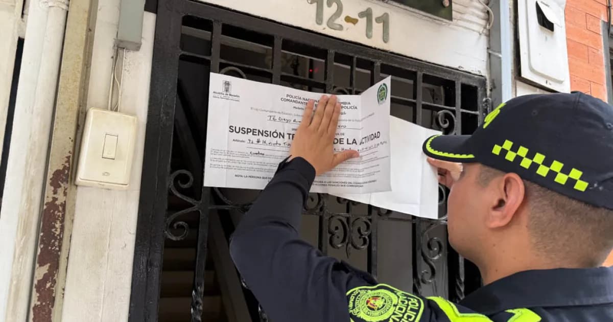 Un policía fija un aviso de suspensión temporal de actividad en la puerta de una vivienda de Medellín