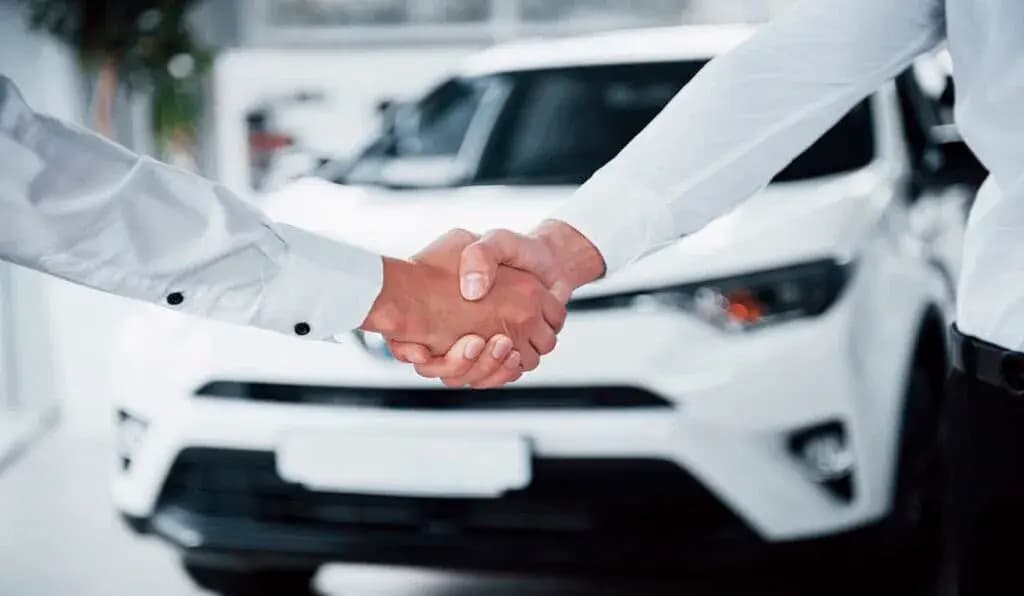 Dos personas se dan la mano frente a un automóvil blanco en el salón de exhibición de un concesionario