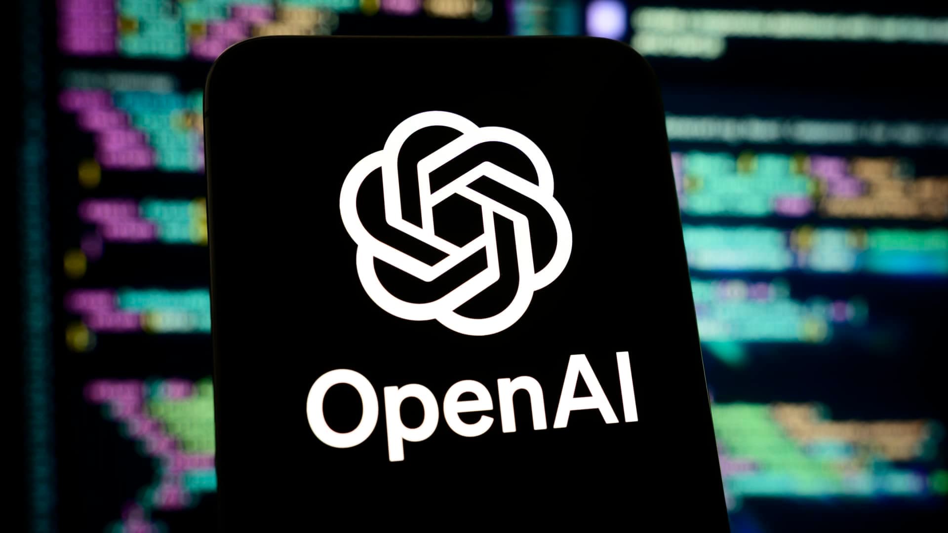 Logotipo de OpenAI en la pantalla de un teléfono, con código de programación al fondo