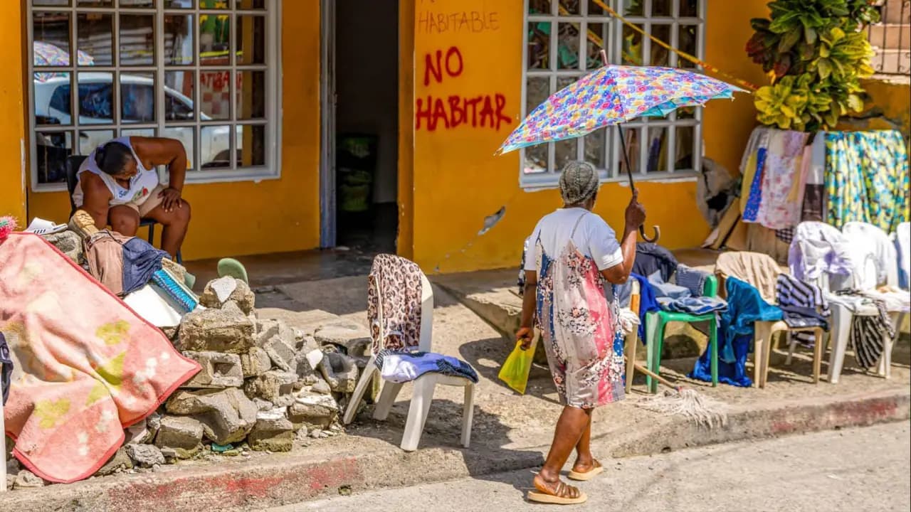 Una mujer camina frente a una casa marcada con la pintada «No habitar», entre escombros y enseres sacados a la calle en el Chocó