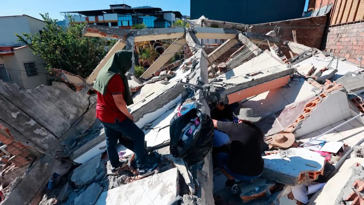 Dos personas rescatan enseres entre los escombros de una vivienda derrumbada
