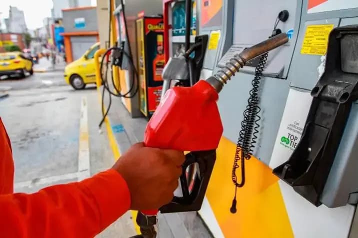 Un empleado de estación de servicio sostiene la pistola surtidora de gasolina frente a un dispensador