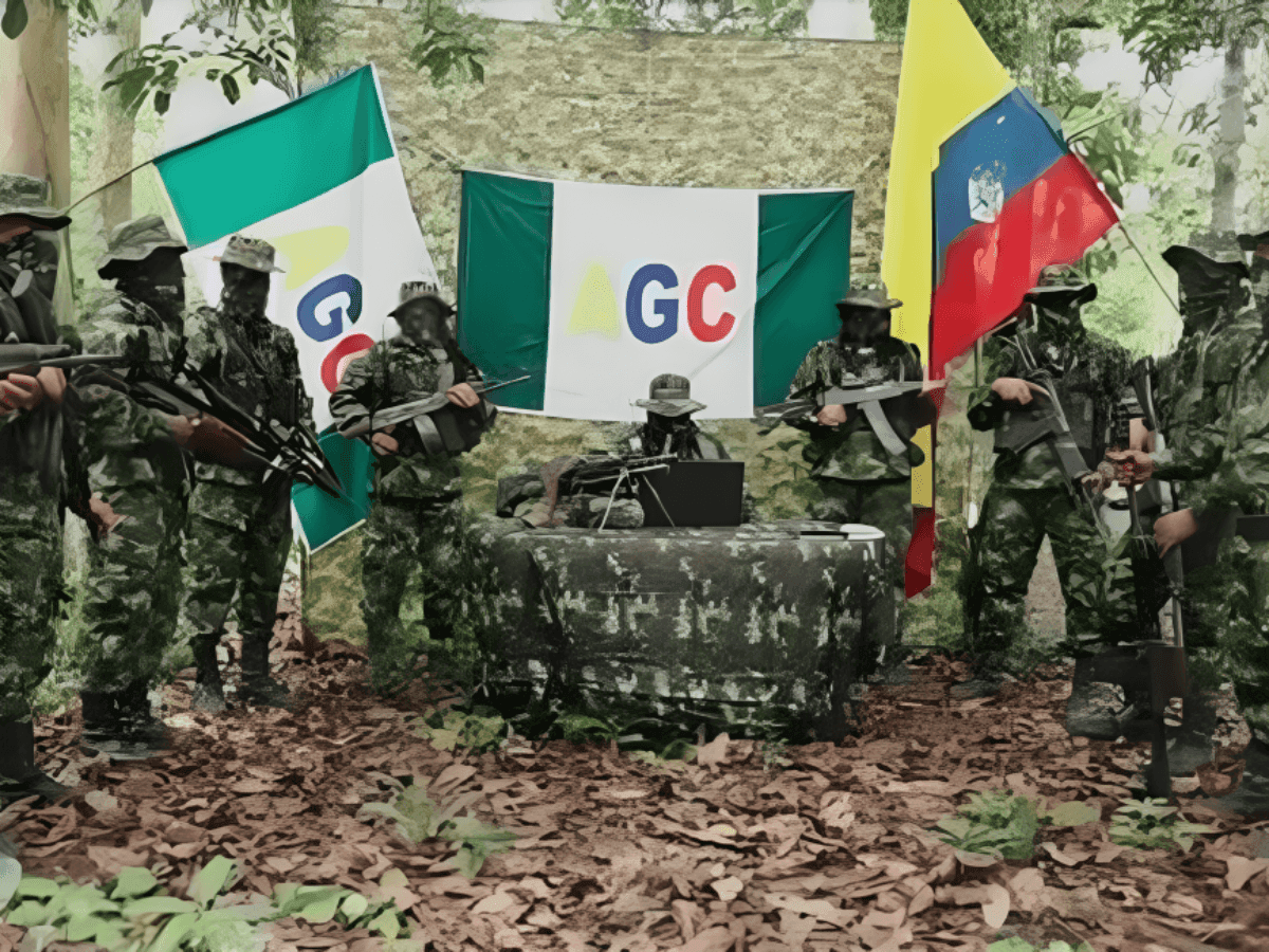 Hombres armados y encapuchados con uniforme camuflado posan en un claro de selva ante banderas con la sigla AGC