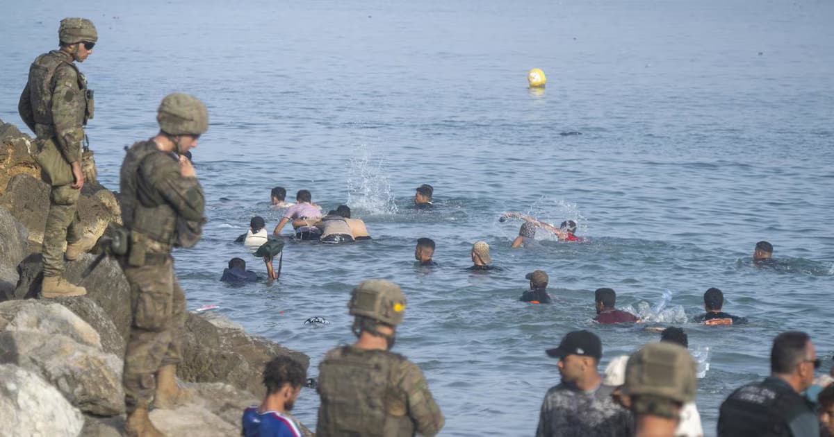 Soldados españoles vigilan desde las rocas a migrantes que nadan hacia la costa de Ceuta