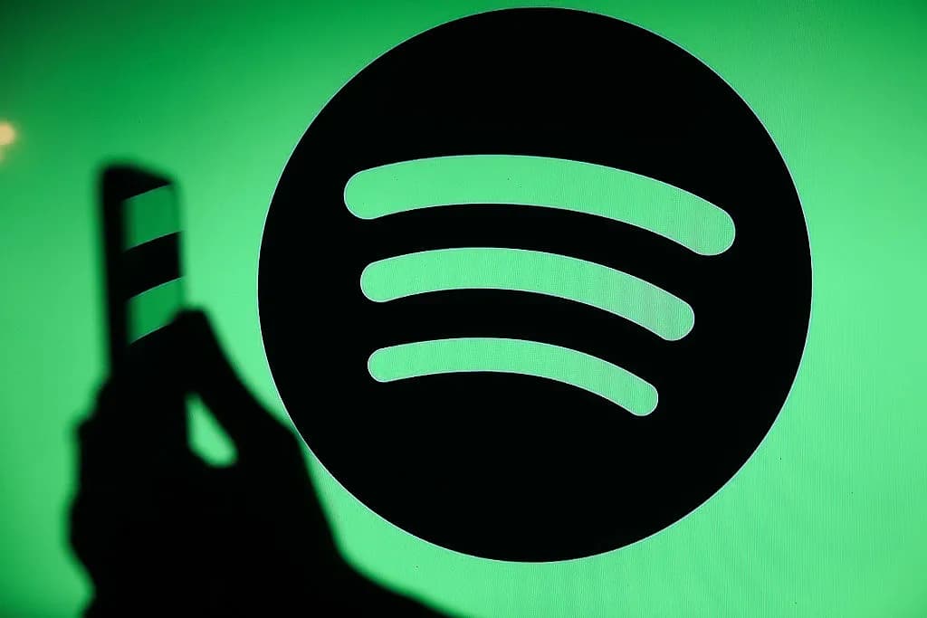 Silueta de una mano con un teléfono frente al logotipo de Spotify