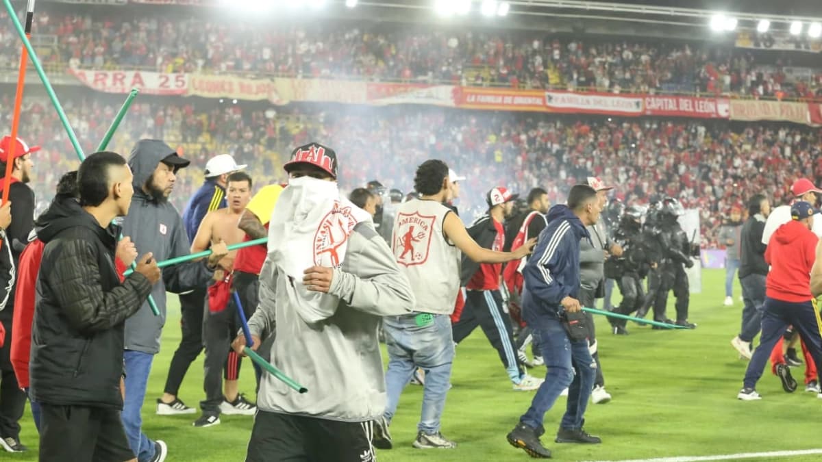 Hinchas invaden el césped del estadio El Campín con palos en las manos mientras la Policía antidisturbios avanza al fondo