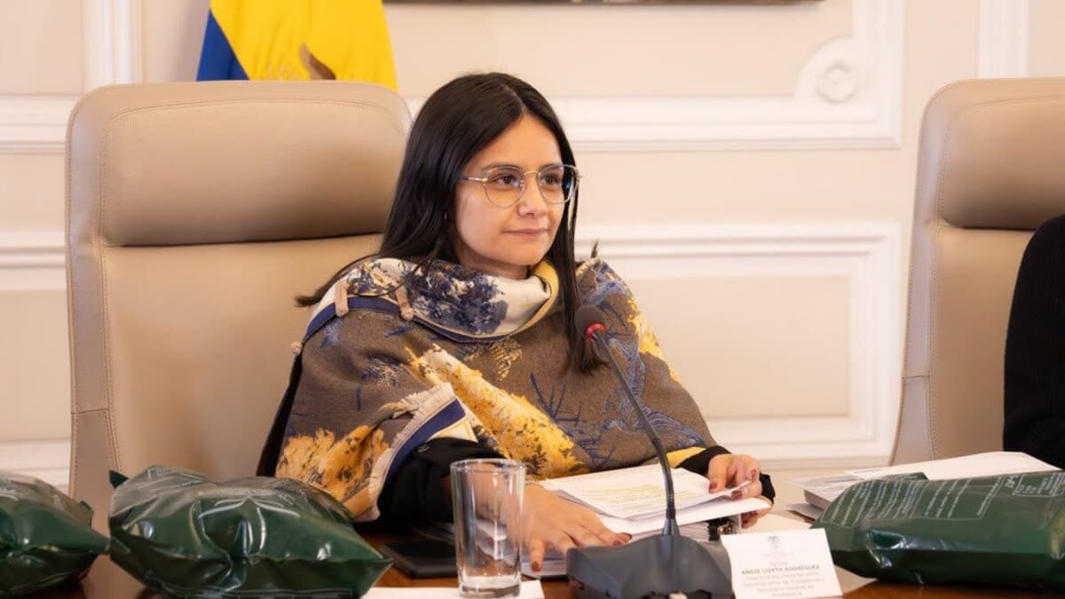 Angie Rodríguez, con gafas y ruana estampada, sentada frente a un micrófono en una mesa de reuniones oficial