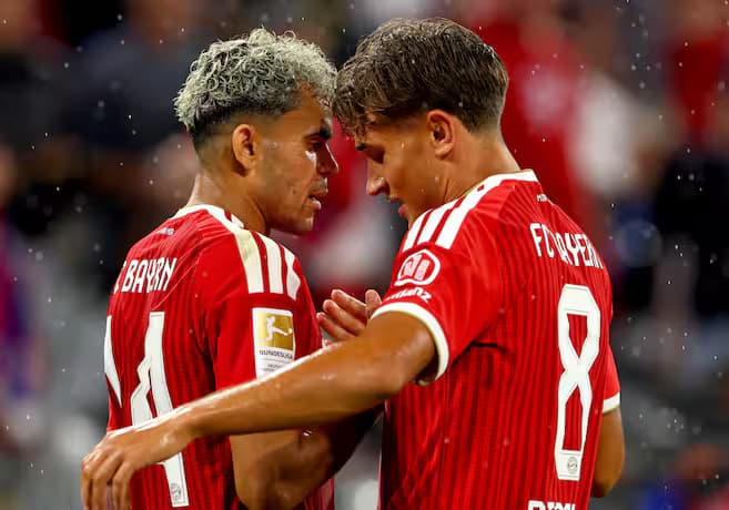 Luis Díaz, de camiseta roja del Bayern Múnich, celebra con un compañero sobre el césped