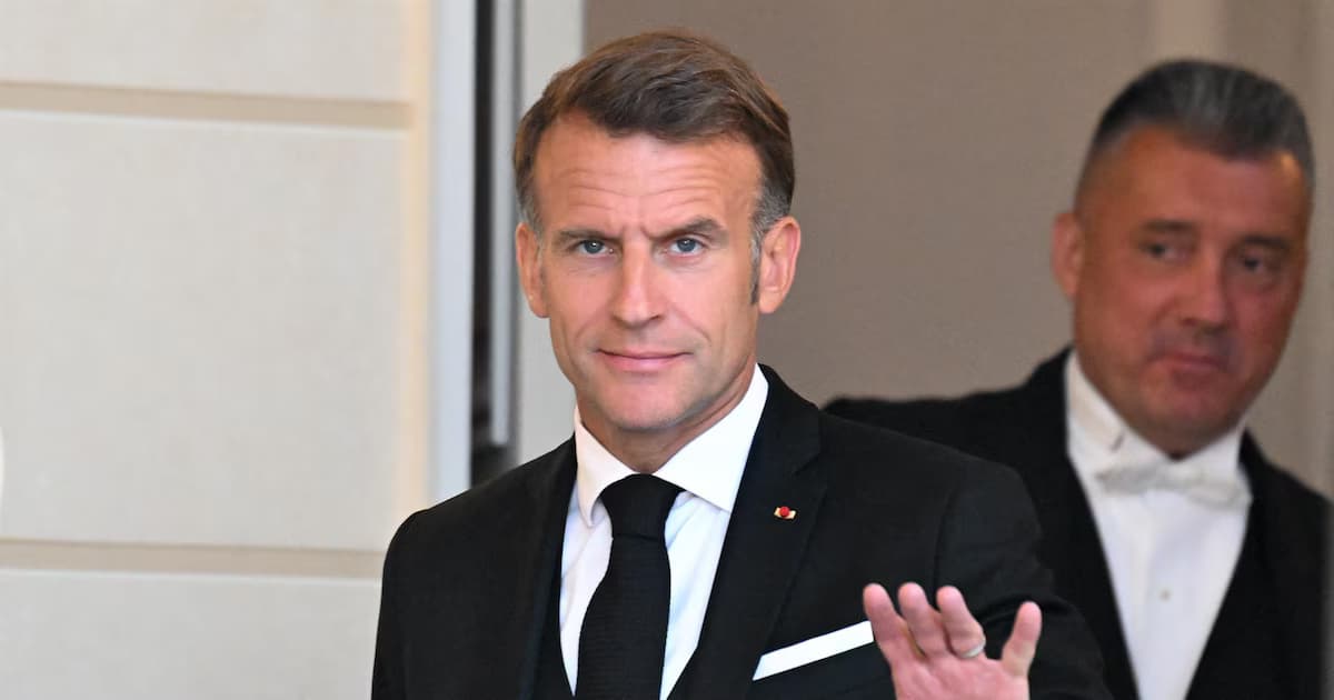 El presidente francés Emmanuel Macron, de esmoquin, saluda con la mano al entrar a un salón acompañado por un hombre de frac