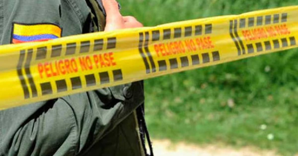 Un policía de uniforme verde detrás de una cinta amarilla de acordonamiento con la leyenda «Peligro no pase»