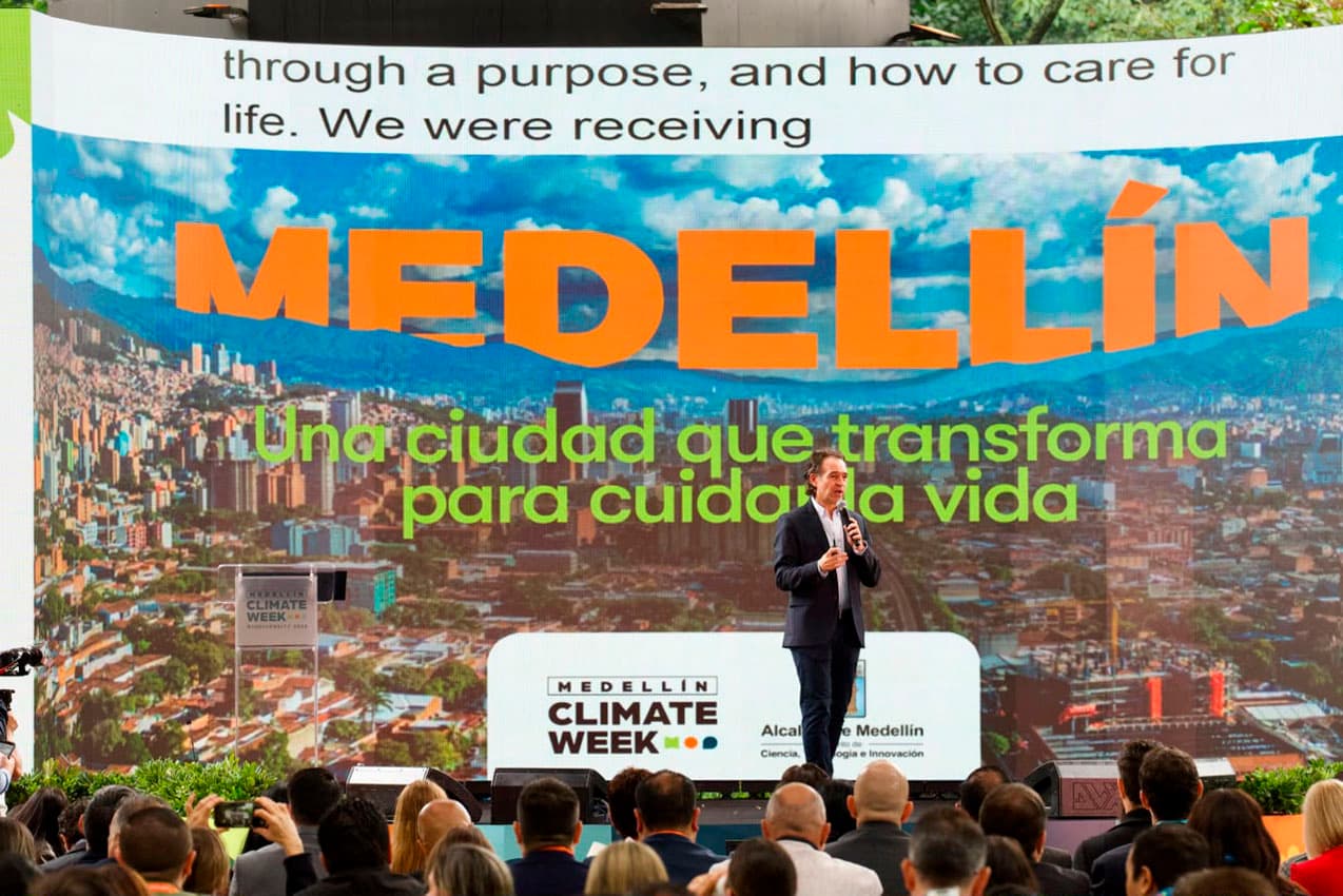 Federico Gutiérrez habla en el escenario de la Climate Week de Medellín ante el público, frente a una pantalla con una panorámica de la ciudad