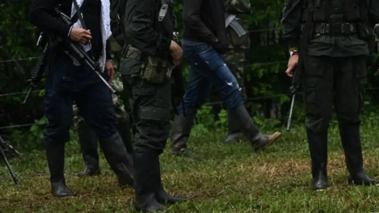 Cuatro hombres armados con fusiles y botas de caucho caminan por un potrero junto a una cerca de alambre