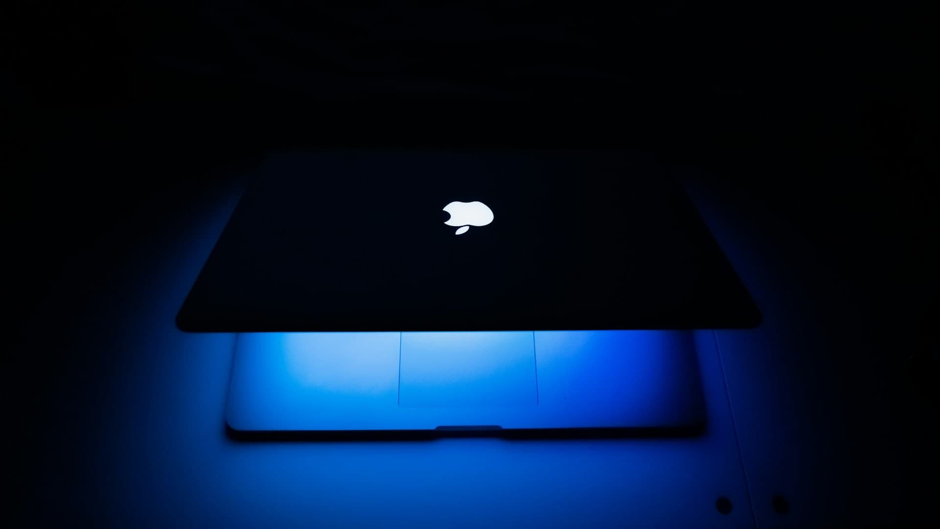 Un MacBook entreabierto ilumina de azul la superficie sobre la que reposa