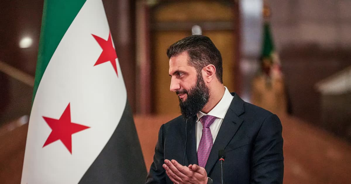 El presidente de transición sirio, Ahmed al Shara, habla junto a la bandera de Siria