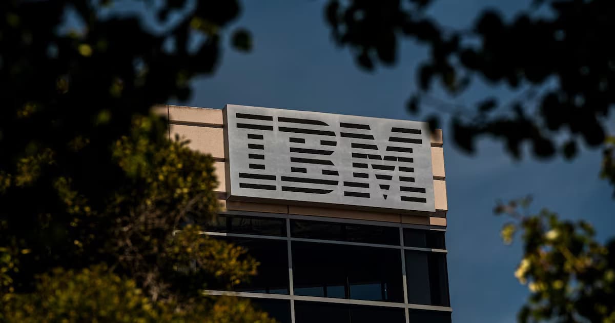Logotipo de IBM en lo alto de un edificio de oficinas, enmarcado por ramas de árboles