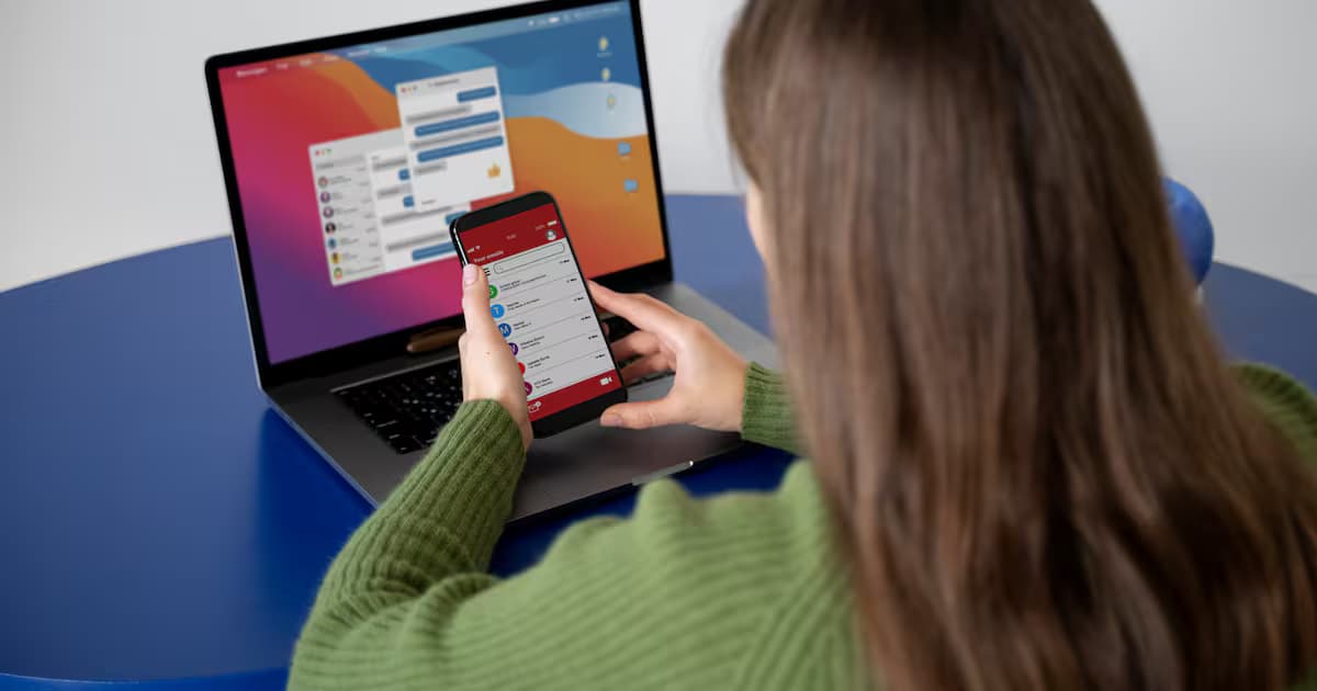 Una mujer usa su teléfono celular frente a un computador portátil
