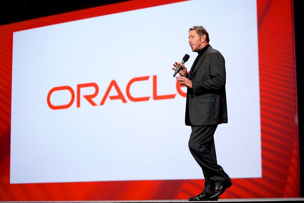 Larry Ellison habla con un micrófono en un escenario frente a una pantalla con el logotipo de Oracle