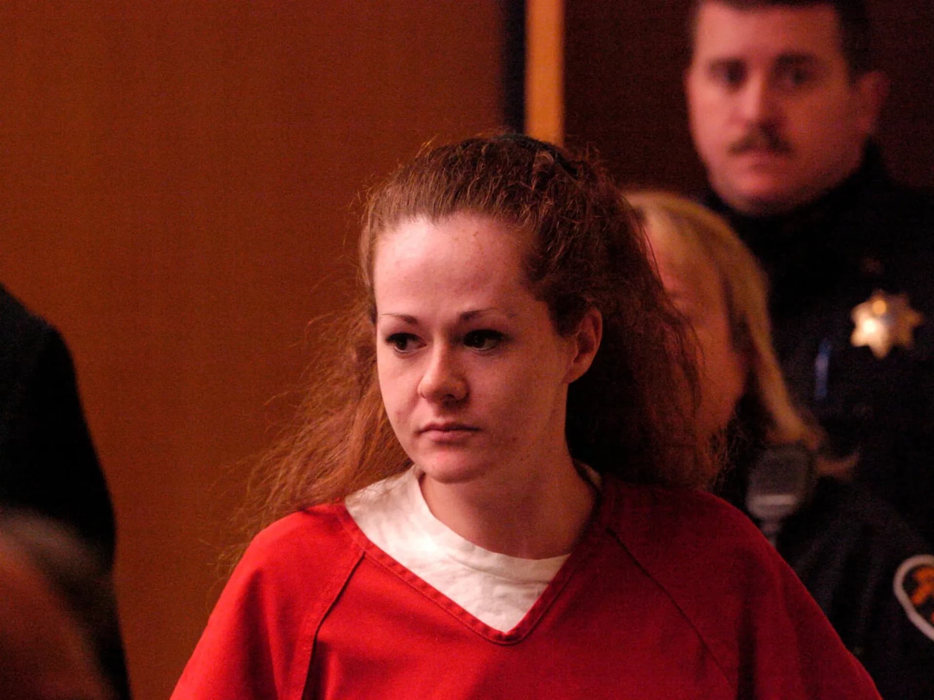Christa Pike, con uniforme rojo de reclusa, en una sala judicial custodiada por un agente
