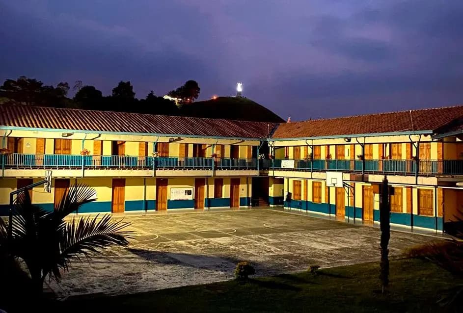 Patio interior de la Escuela Normal Superior de Jericó al anochecer, con el Cristo del cerro iluminado al fondo