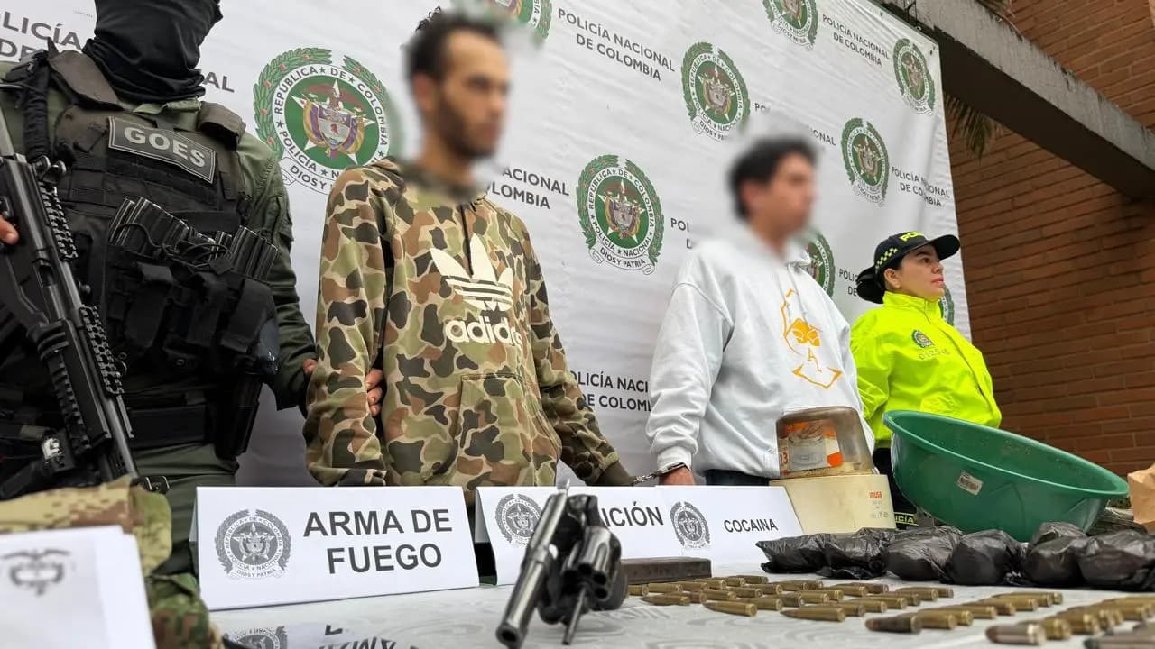 Dos capturados con el rostro difuminado junto a policías y una mesa con un revólver, munición y droga incautada
