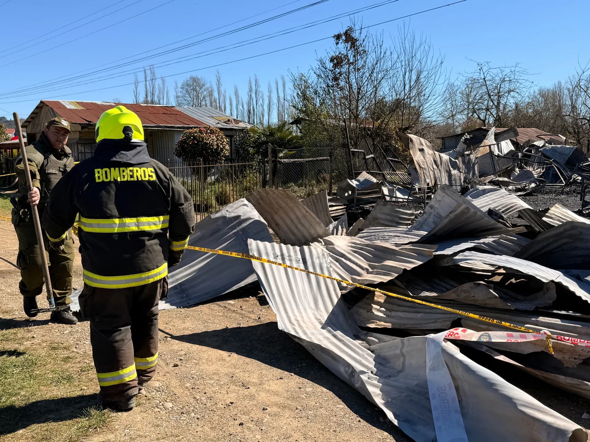 Un bombero y un carabinero junto a las láminas de zinc que quedaron del hogar de ancianos incendiado en Pitrufquén