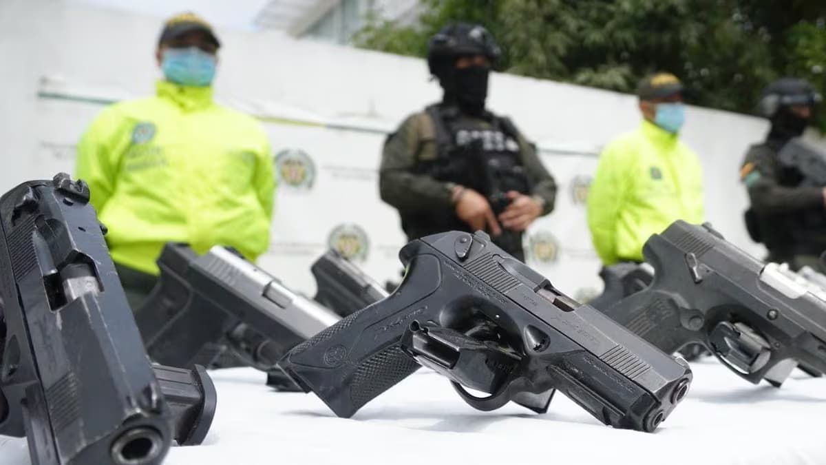 Pistolas incautadas sobre una mesa, con agentes de la Policía al fondo