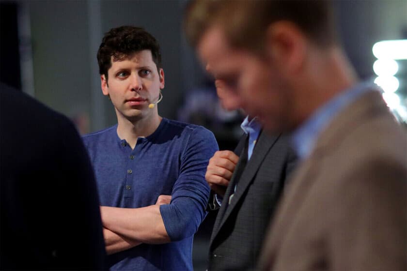 Sam Altman, con jersey azul y micrófono de diadema, cruzado de brazos entre bambalinas durante un acto público