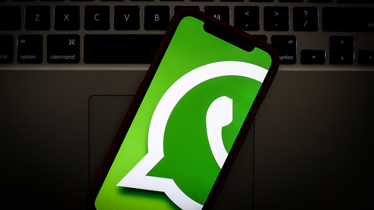 Un teléfono con el logo de WhatsApp en pantalla, apoyado sobre el teclado de un computador portátil