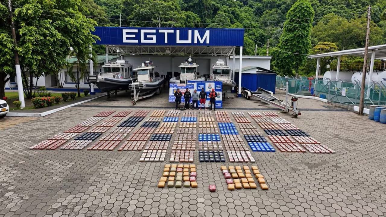 Paquetes de droga incautados extendidos frente a una estación de guardacostas de la Armada, con los tres capturados al fondo