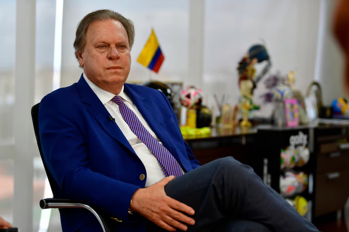 Ramón Jesurún, de saco azul y corbata a rayas, sentado en su oficina frente a una vitrina con balones y trofeos