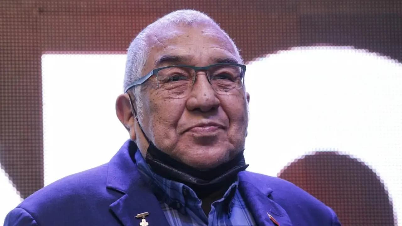 Alci Acosta, de cabello blanco y gafas, sonríe con saco azul durante un acto público
