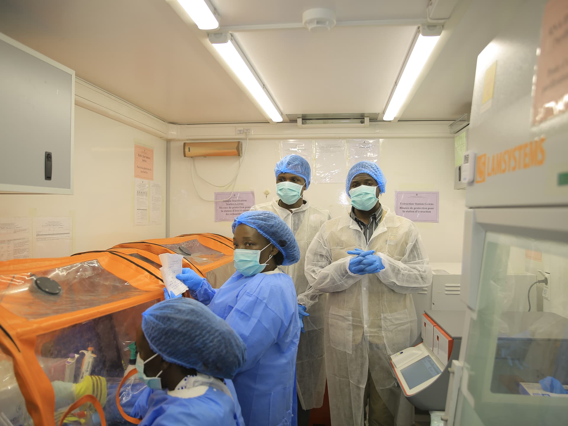 Personal de salud con tapabocas y batas trabaja en un laboratorio móvil de diagnóstico de ébola