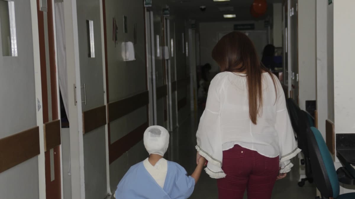 Un niño con vendaje en la cabeza camina de la mano de una mujer por el pasillo de un hospital