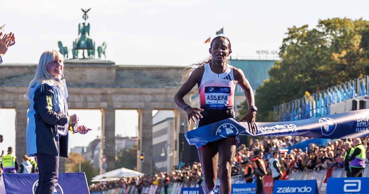 Tigst Assefa cruza la meta del maratón de Berlín frente a la Puerta de Brandeburgo
