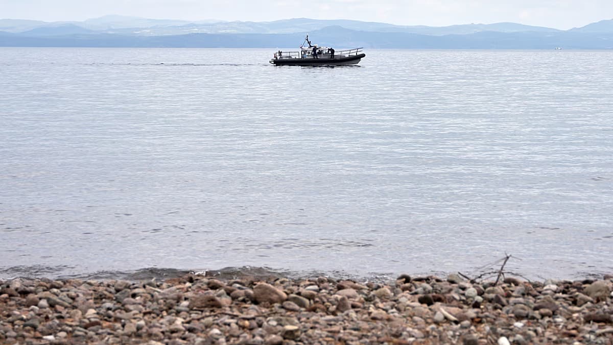 Una lancha patrulla navega frente a una playa de piedras en aguas del Mediterráneo