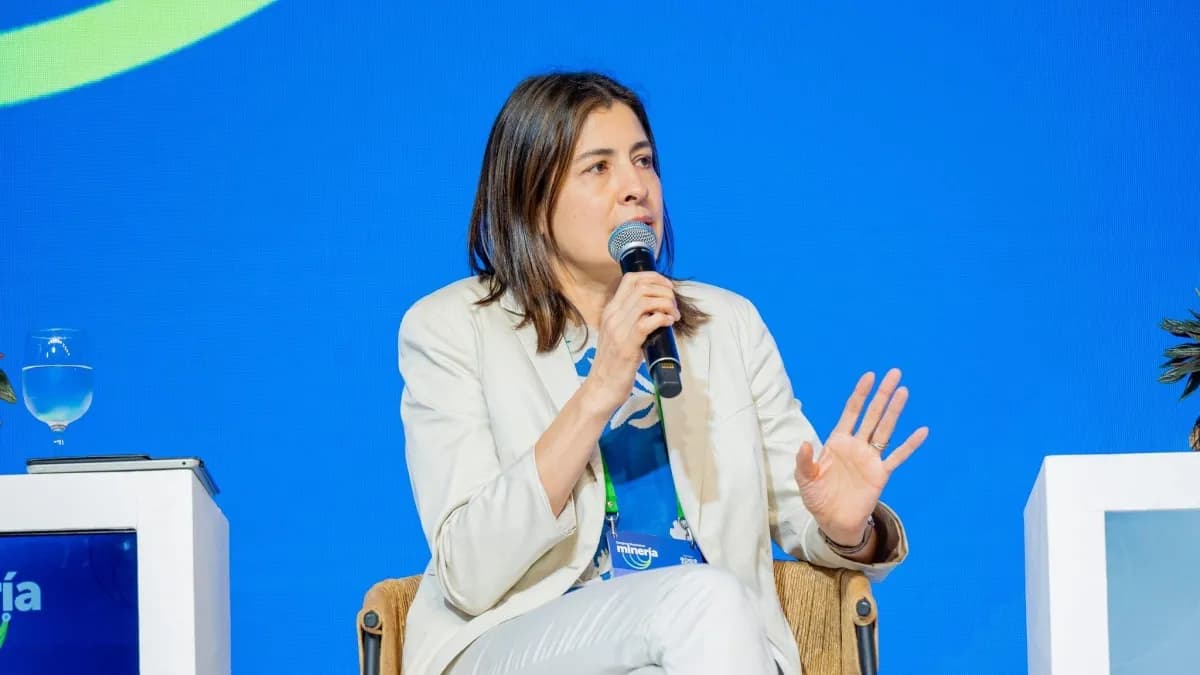 Carolina Soto habla con un micrófono en la mano durante un panel, sentada frente a un fondo azul