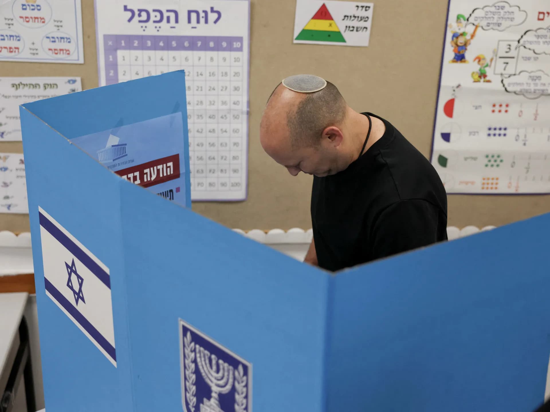 El exprimer ministro israelí Naftali Bennett vota en un cubículo electoral con la bandera de Israel