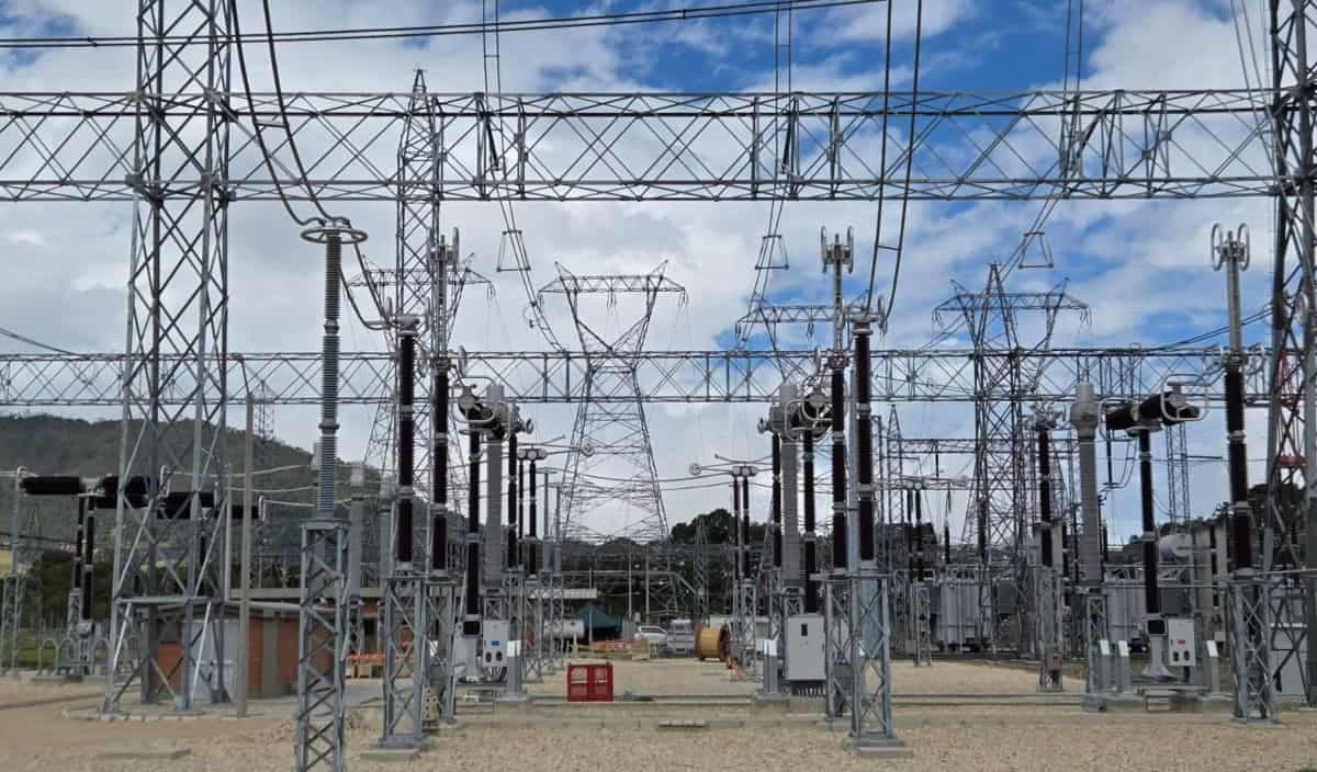 Patio de una subestación eléctrica con torres, aisladores y líneas de alta tensión bajo un cielo nublado