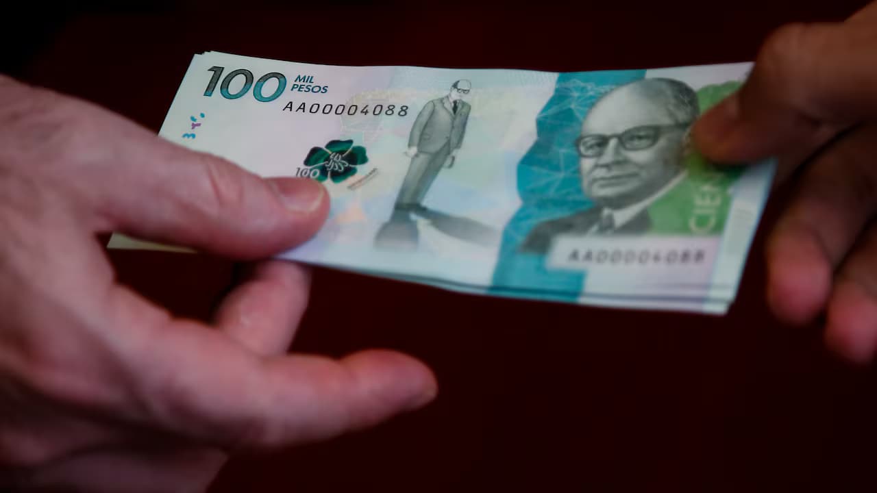 Dos manos sostienen billetes de 100.000 pesos colombianos