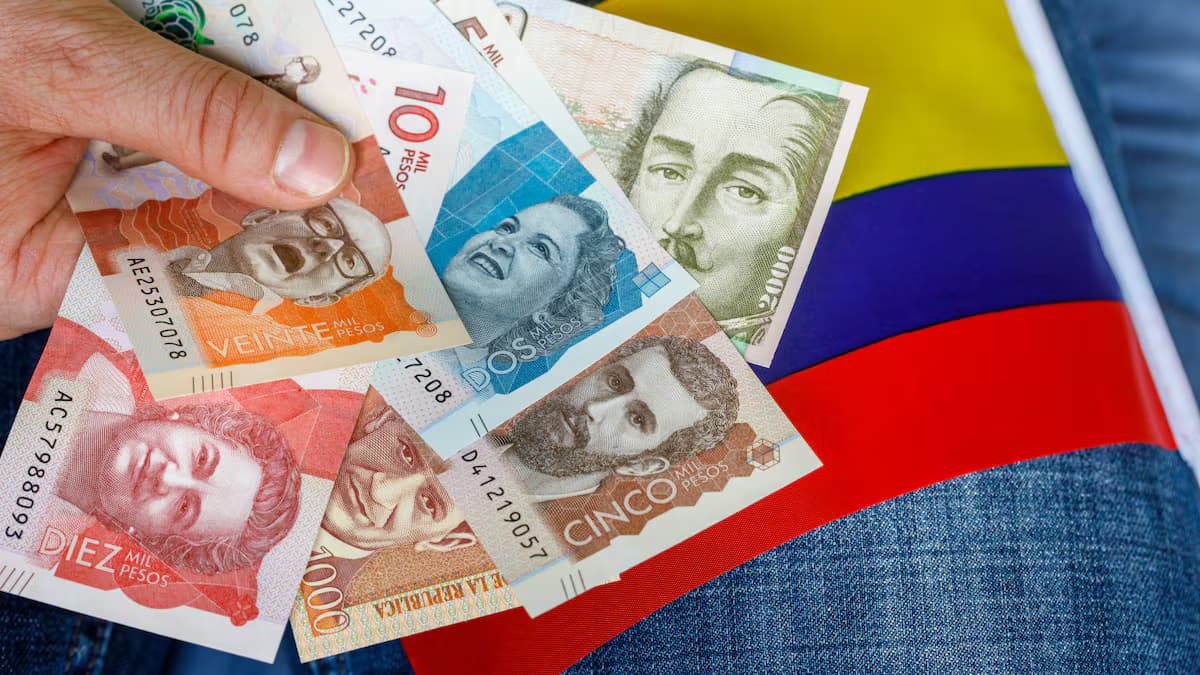 Billetes colombianos de varias denominaciones sobre una bandera de Colombia